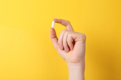 Photo of Woman holding vitamin capsule on yellow background, closeup. Space for text