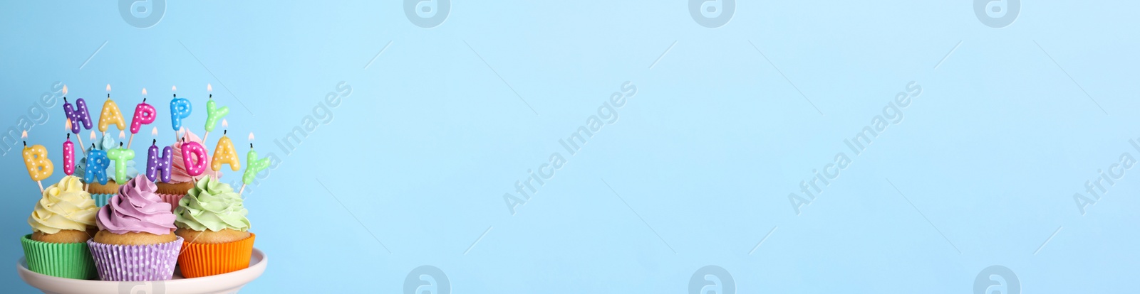 Photo of Birthday cupcakes with burning candles on stand against light blue background. Space for text