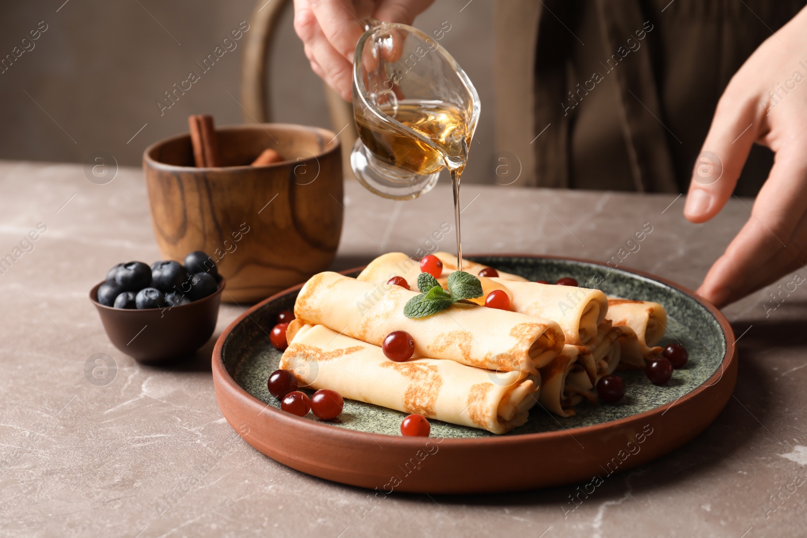 Photo of Woman pouring honey onto thin pancakes with berries at table