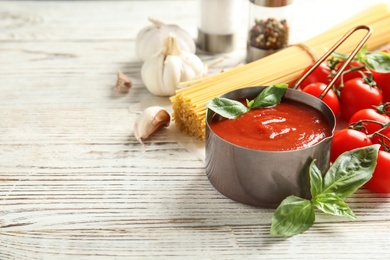 Photo of Pan of tasty tomato sauce served on wooden table. Space for text