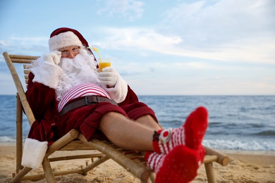 Photo of Santa Claus with cocktail relaxing on beach. Christmas vacation
