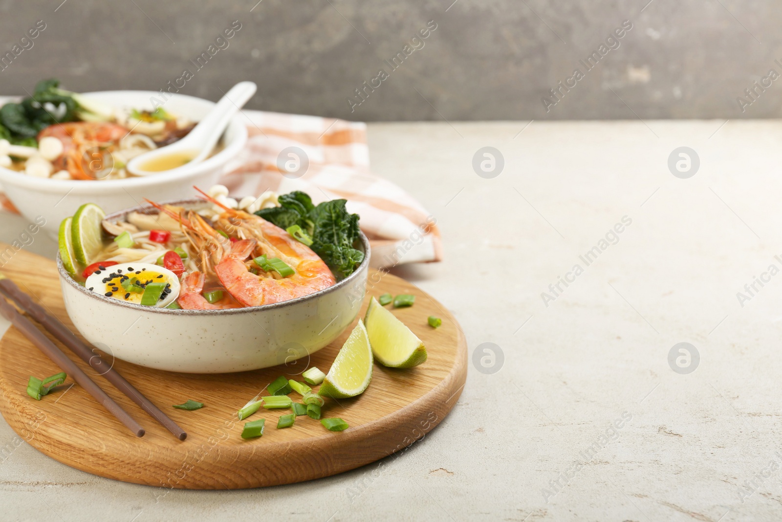 Photo of Delicious ramen with shrimps, egg in bowl and chopsticks on light textured table, space for text. Noodle soup