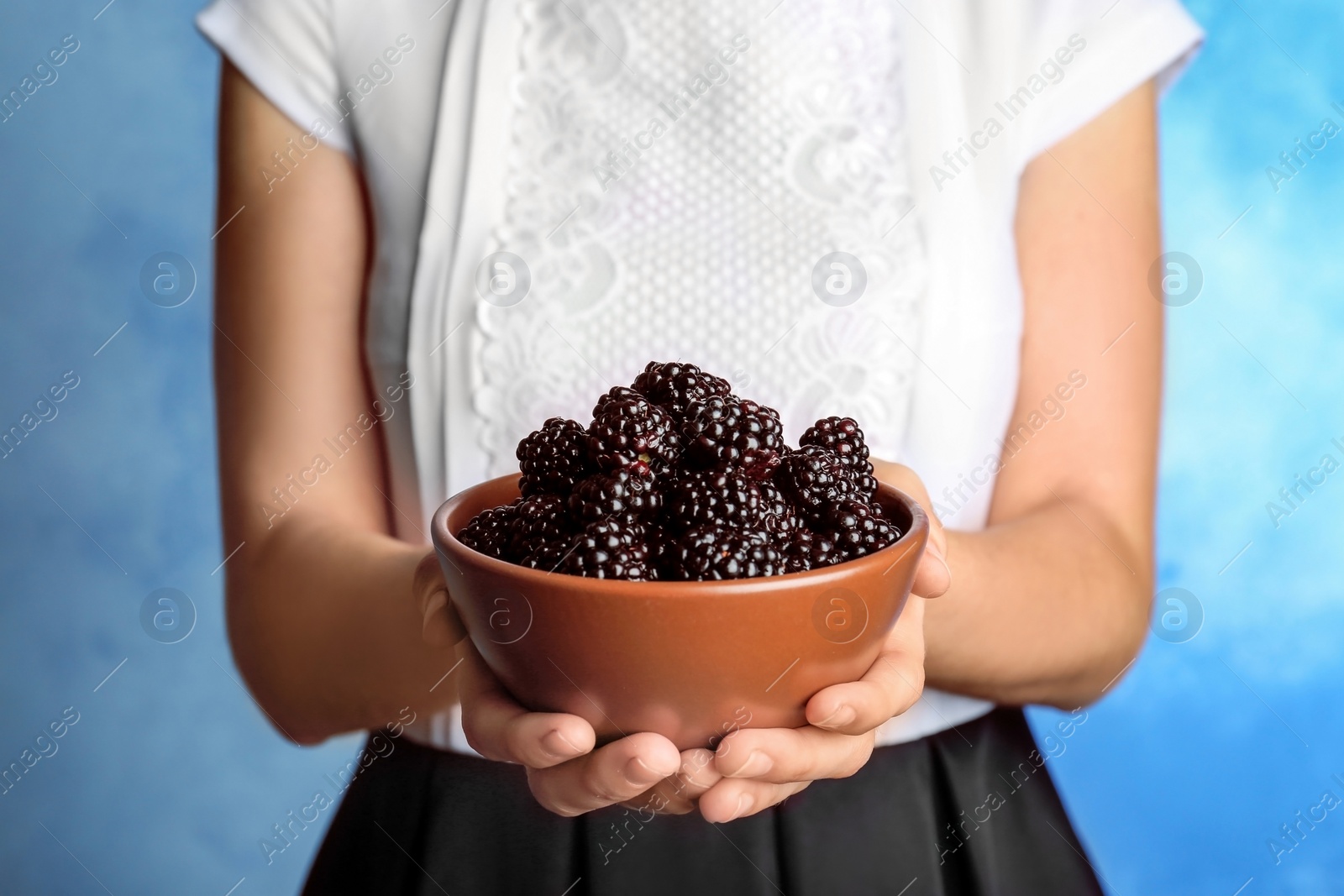 Photo of Woman holding bowl of fresh blackberry against color background, closeup