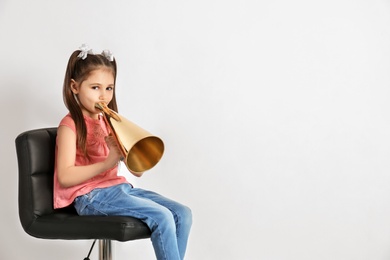 Cute little girl with megaphone sitting against white background