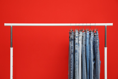 Rack with stylish jeans on red background