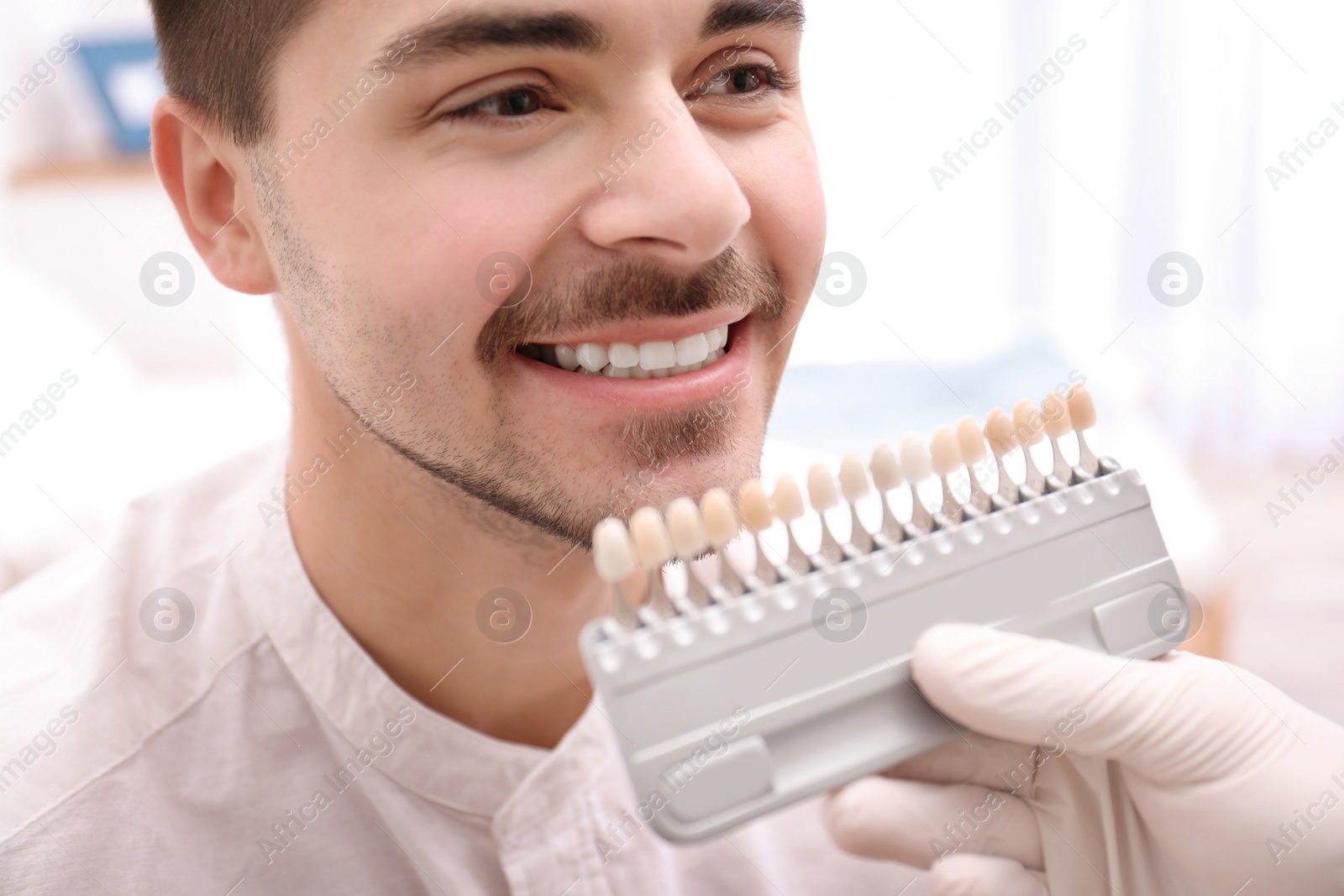 Photo of Dentist checking young man's teeth color, closeup