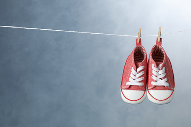 Photo of Child's shoes hanging on laundry line against dark background, space for text