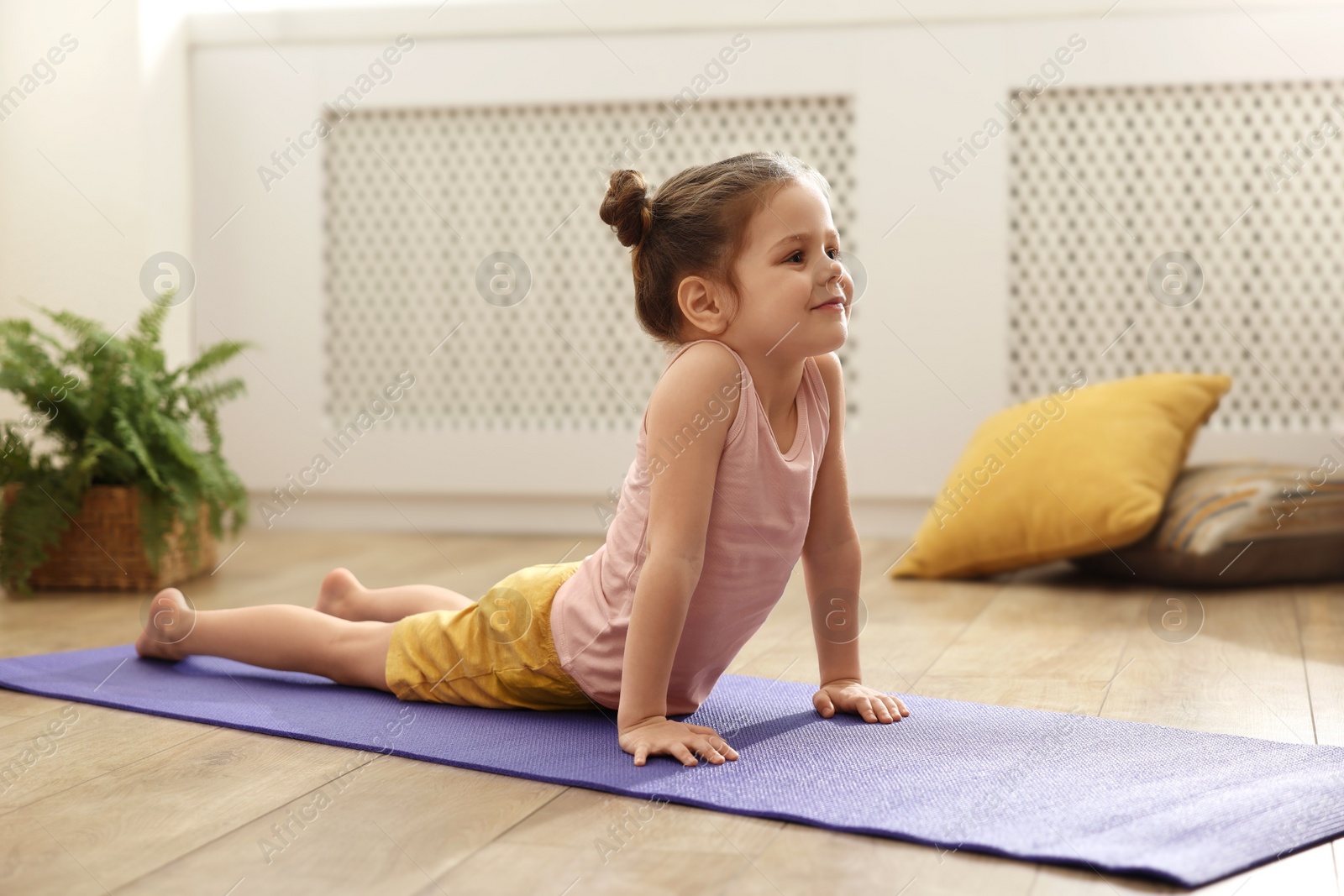 Photo of Little cute girl practicing yoga on mat at home