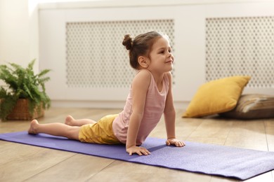 Little cute girl practicing yoga on mat at home