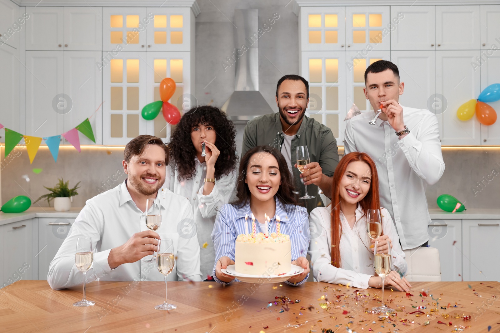 Photo of Happy friends with tasty cake celebrating birthday in kitchen