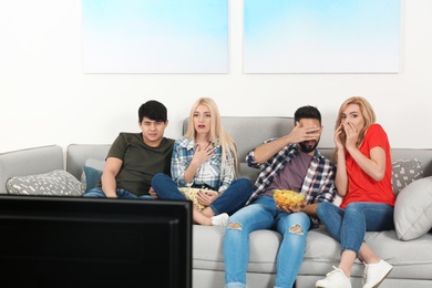 Young people with snacks watching TV on sofa at home