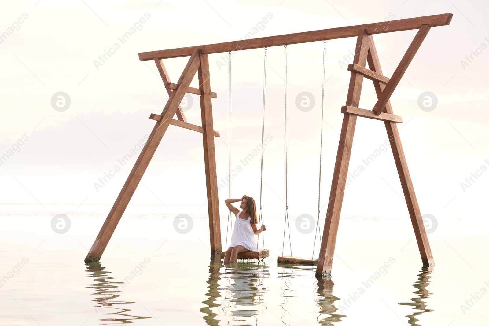 Photo of Young woman enjoying sunrise on swing over water