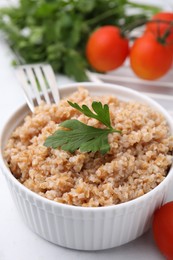 Photo of Tasty wheat porridge with parsley and tomatoes in bowl on white table, closeup