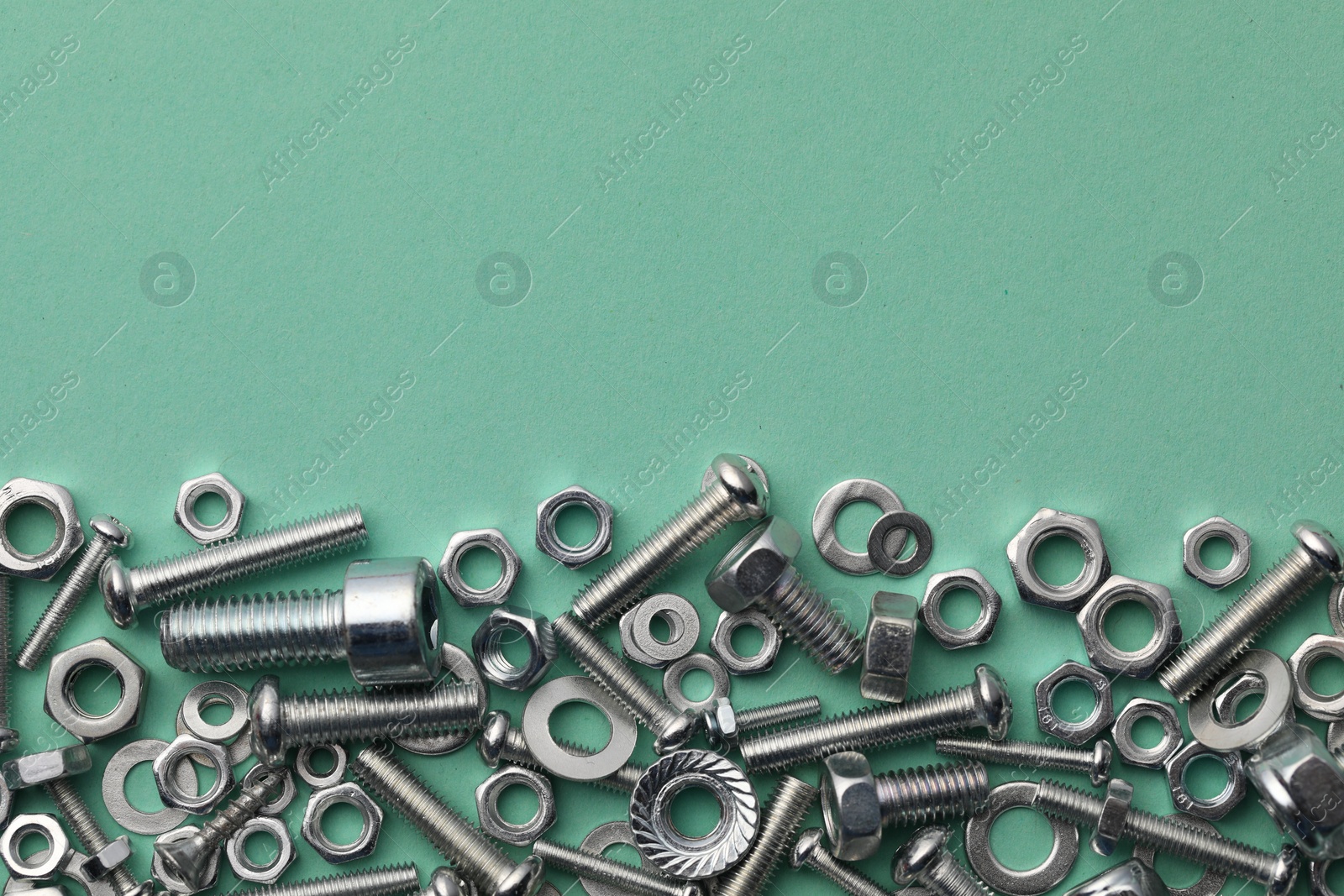 Photo of Different metal bolts and nuts on turquoise background, flat lay. Space for text