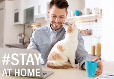 Image of Hashtag Stay At Home - protective measure during coronavirus pandemic. Man with cute cat working on laptop in kitchen
