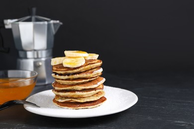 Photo of Plate of banana pancakes with honey and powdered sugar served on black table. Space for text