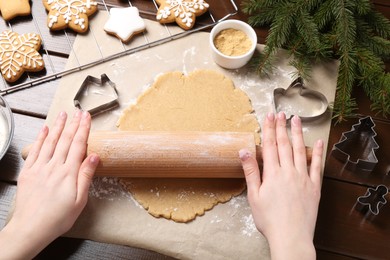 Photo of Making Christmas cookies. Woman rolling raw dough at wooden table, top view