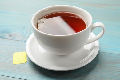 Photo of Tea bag in cup with hot drink on light blue wooden table, closeup