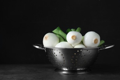 Photo of Colander with green spring onions on black table, space for text