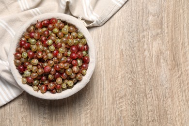 Photo of Fresh ripe gooseberries in bowl on wooden table, top view. Space for text