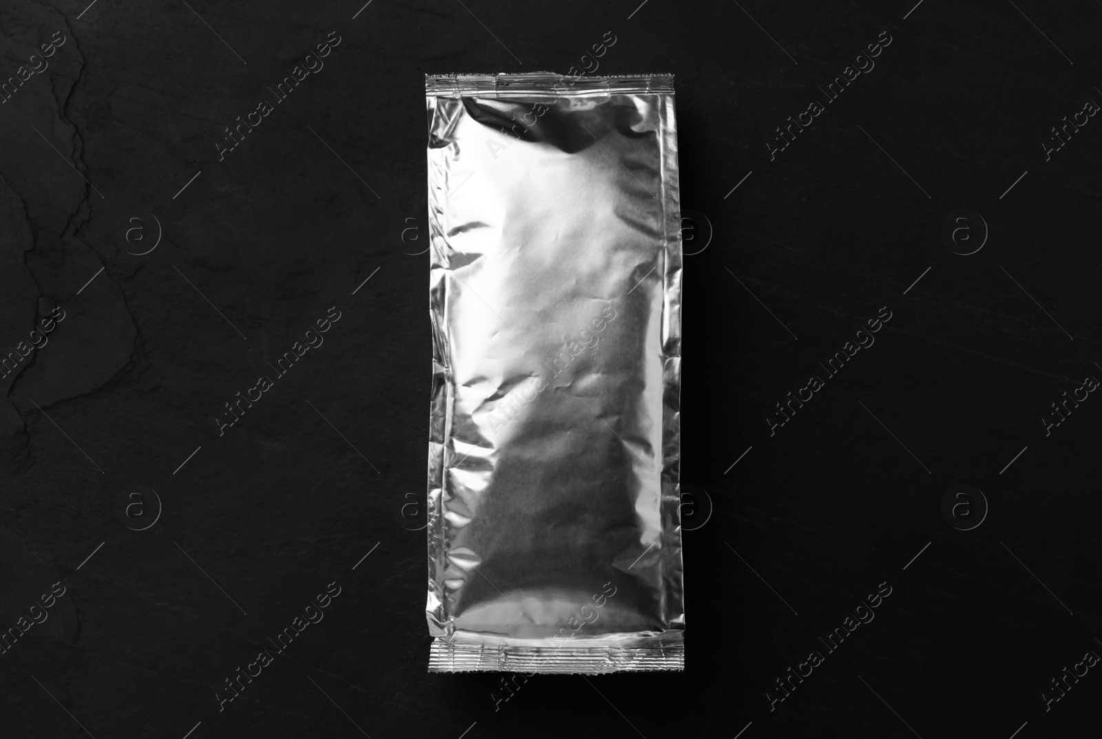 Photo of Blank foil package on black table, top view