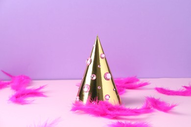 Photo of Golden party hat with rhinestones and bright feathers on color background