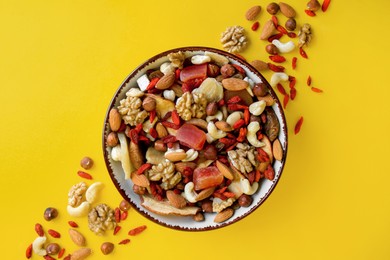 Photo of Bowl with mixed dried fruits and nuts on yellow background, flat lay