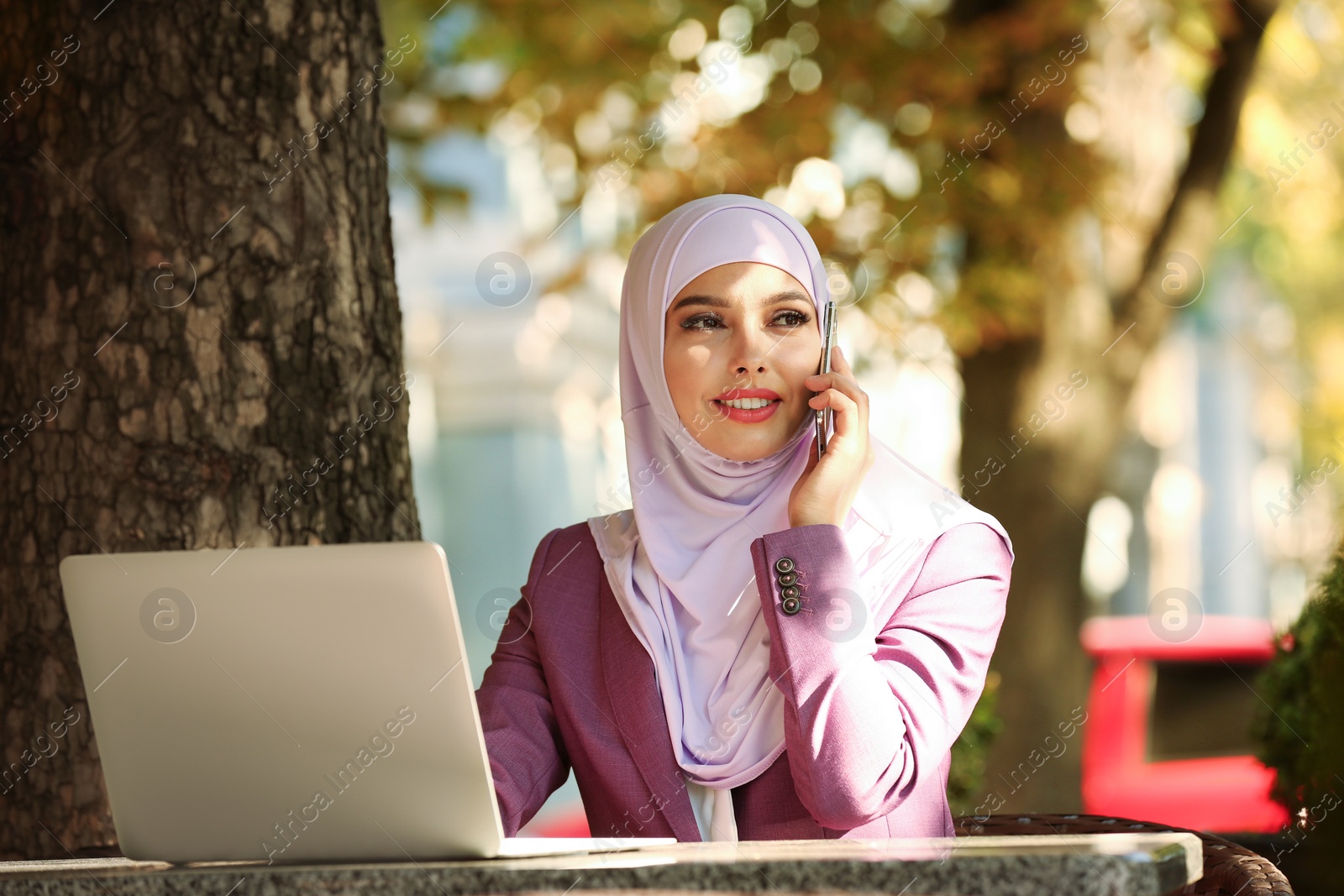 Photo of Muslim woman talking on phone in outdoor cafe