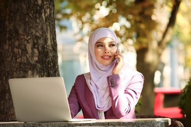 Photo of Muslim woman talking on phone in outdoor cafe