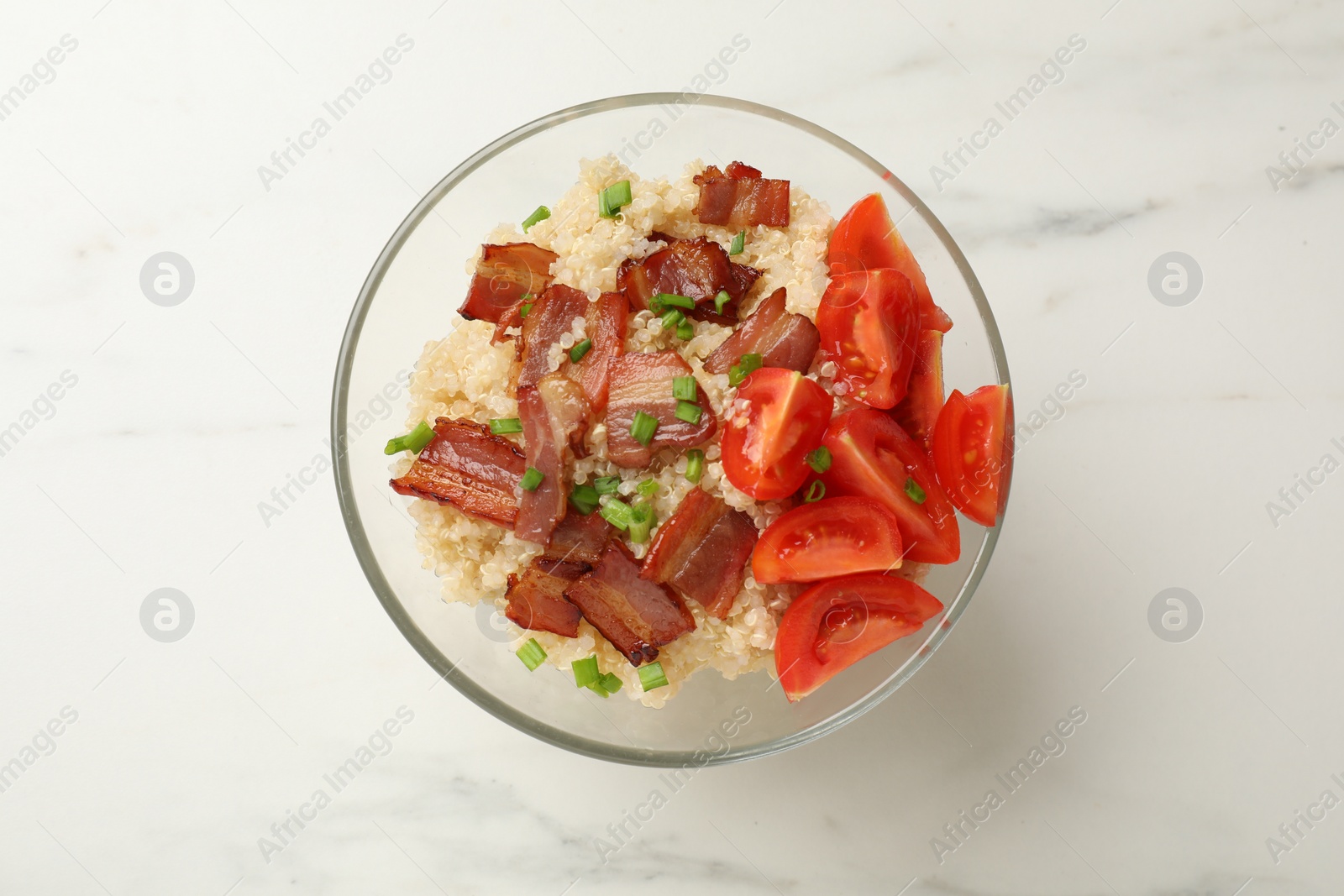 Photo of Tasty quinoa porridge with fried bacon and tomato in bowl on white marble table, top view