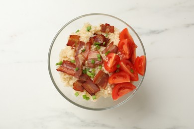 Photo of Tasty quinoa porridge with fried bacon and tomato in bowl on white marble table, top view