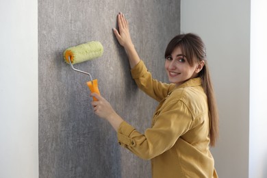 Woman hanging stylish gray wallpaper in room
