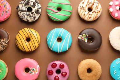 Photo of Sweet tasty glazed donuts on brown background, flat lay