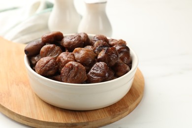 Roasted edible sweet chestnuts in bowl on white table, closeup. Space for text