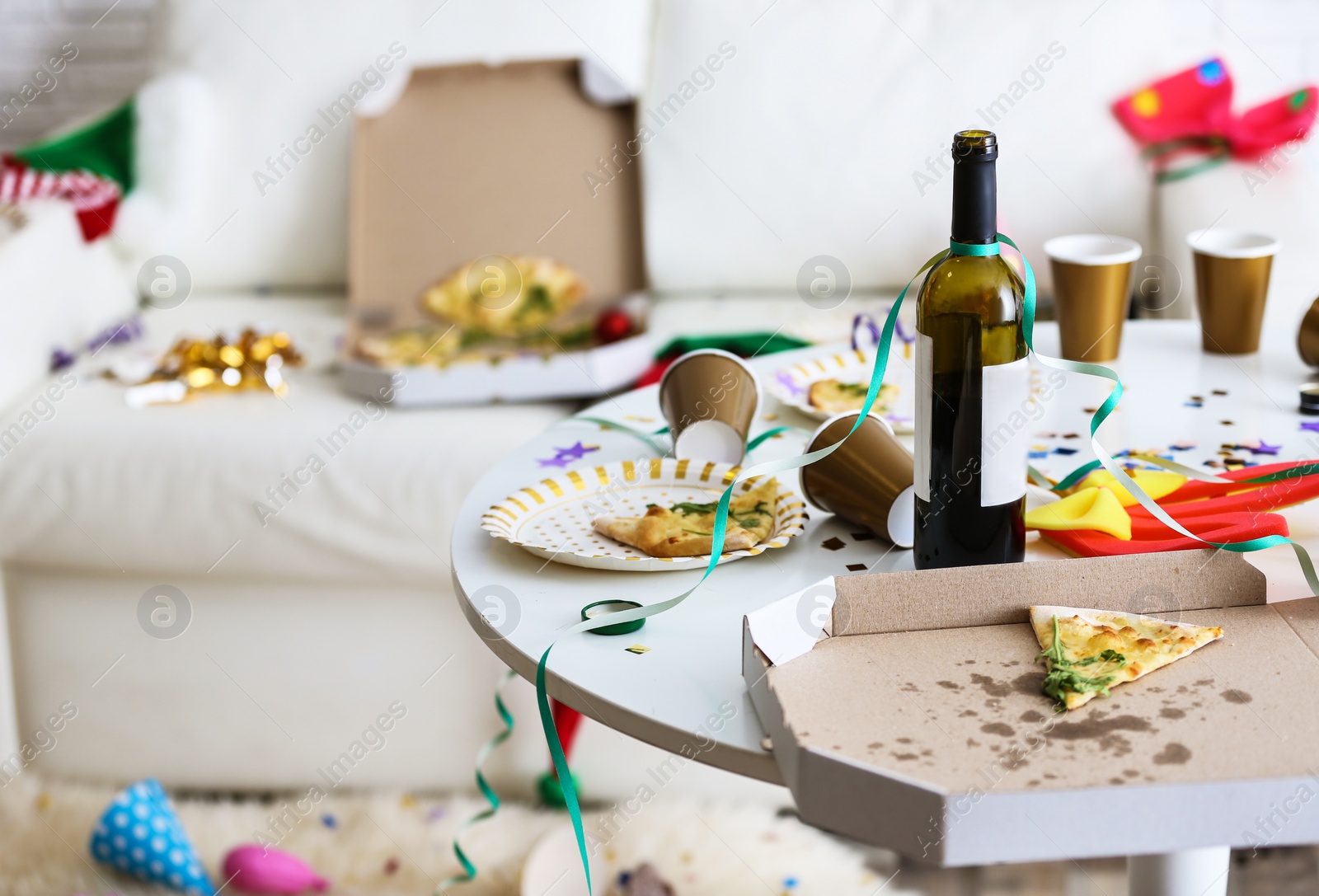 Photo of Messy table with bottle of wine and pizza indoors, space for text. Chaos after party