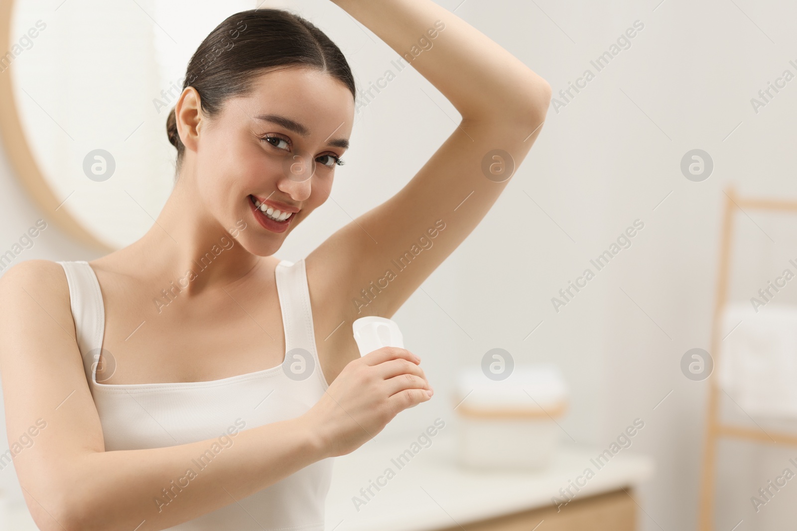 Photo of Beautiful young woman applying deodorant in bathroom