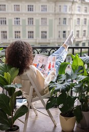 Young woman reading magazine surrounded by green houseplants on balcony