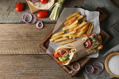 Photo of Delicious pita wrap with meat, vegetables and potato fries on wooden table, flat lay. Space for text