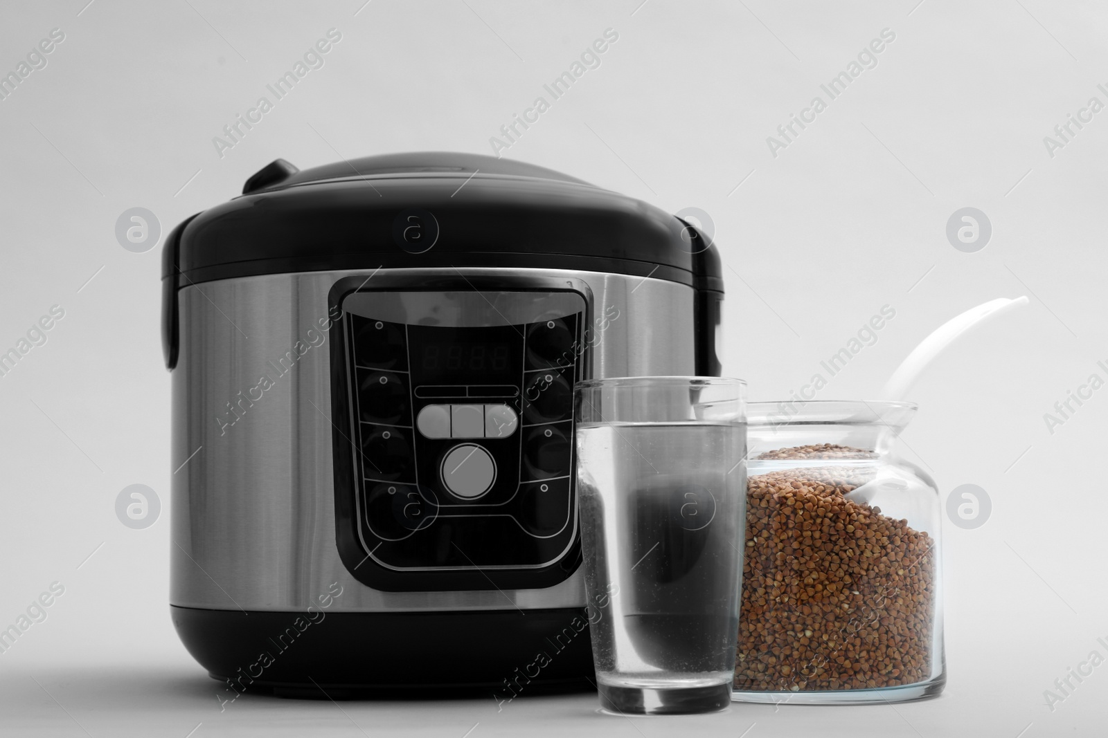 Photo of Modern electric multi cooker, buckwheat and glass of water on grey background
