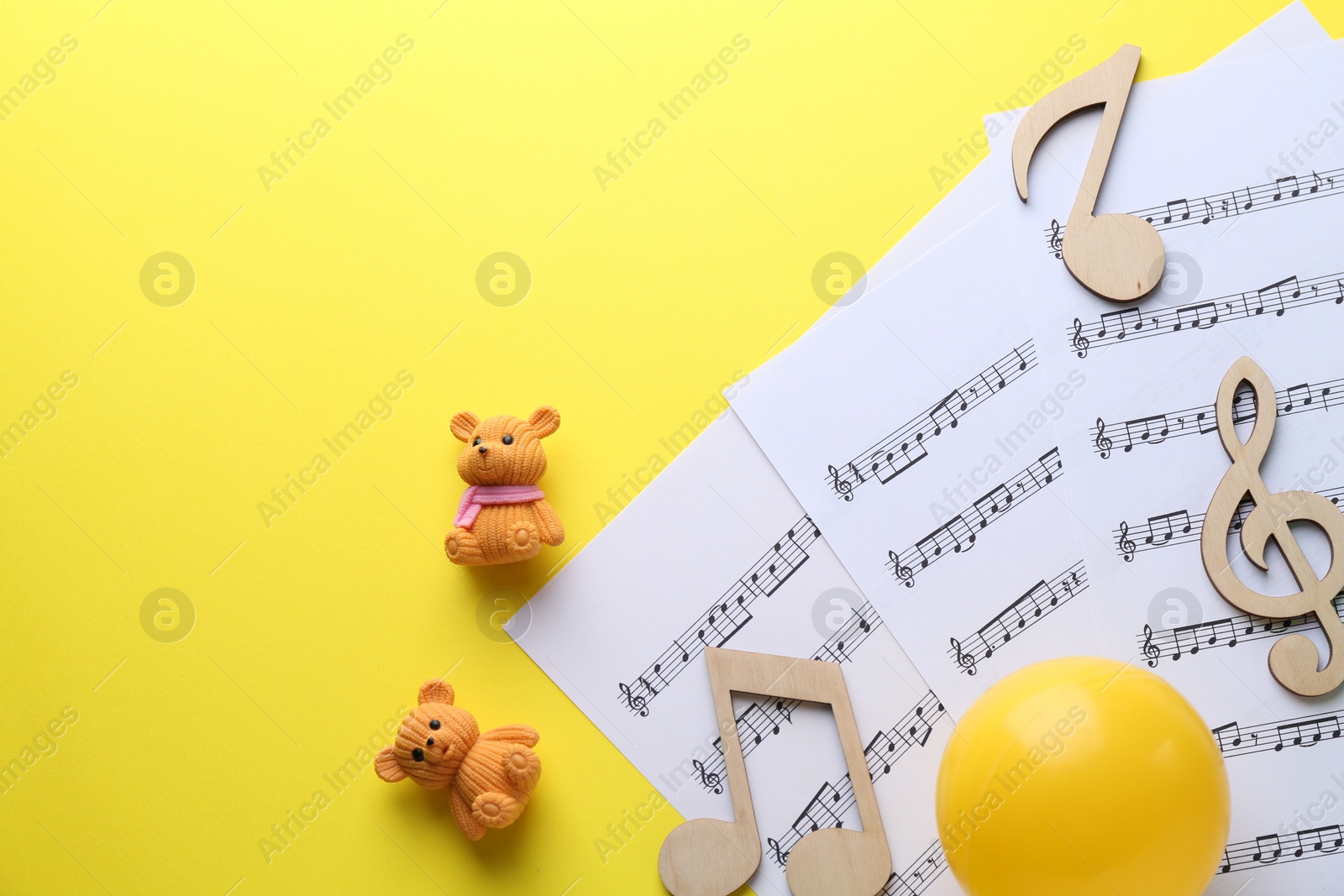 Photo of Baby songs. Music sheets, wooden notes, toy bears and ball on yellow background, top view with space for text