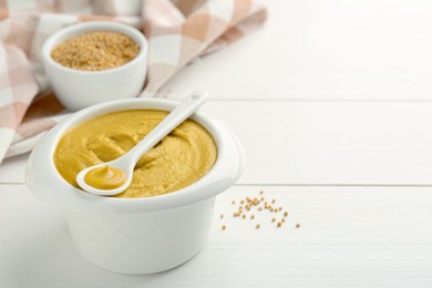 Photo of Bowl and spoon with tasty mustard sauce on white wooden table, closeup. Space for text