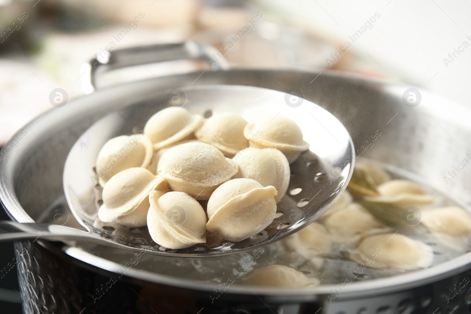 Photo of Closeup of dumplings on skimmer over stewpan with boiling water. Home cooking