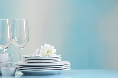 Photo of Set of many clean dishware, flower and glasses on light blue table. Space for text
