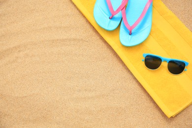 Photo of Yellow towel, sunglasses and flip flops on sand, top view with space for text
