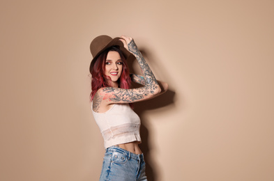 Photo of Beautiful woman with tattoos on body against beige background