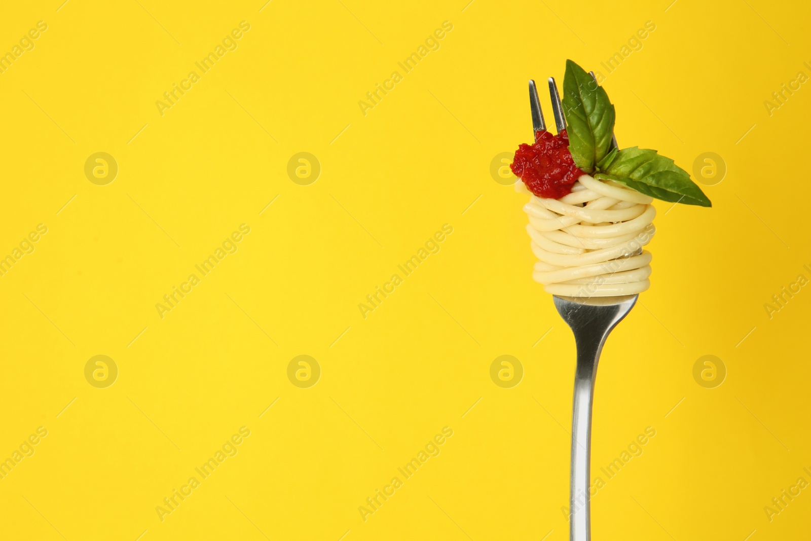 Photo of Fork with tasty pasta, tomato sauce and basil leaves on yellow background, space for text