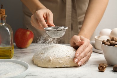 Photo of Woman sprinkling flour onto dough at white marble table, closeup