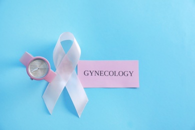 Flat lay composition with symbolic ribbon of breast cancer awareness and wristwatch on color background. Gynecological care