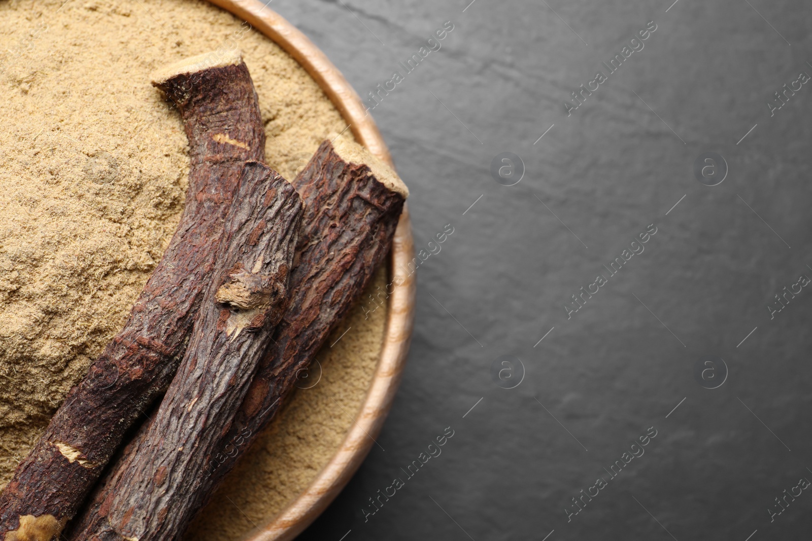 Photo of Powder in bowl and dried sticks of liquorice root on black table, top view. Space for text