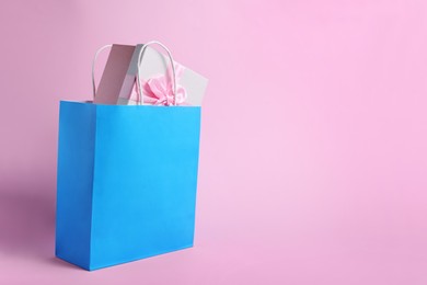 Photo of Light blue paper shopping bag with gift box on pink background. Space for text